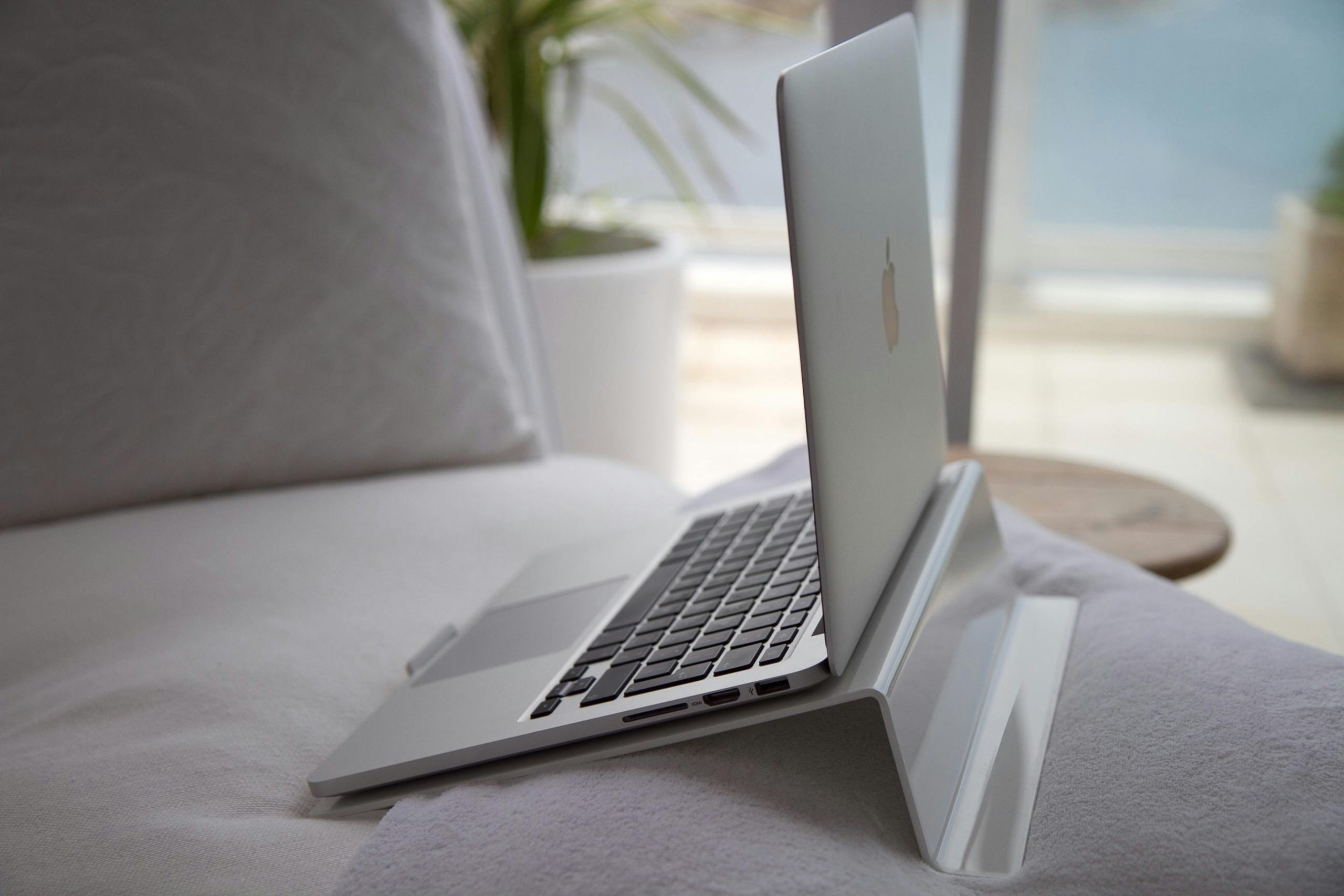 A modern laptop sits open on a cozy couch with natural sunlight streaming in.